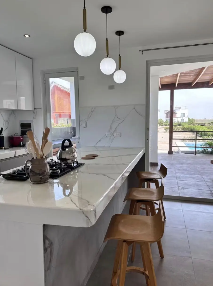 Cocina con isla de mármol, banquetas de madera y salida a la terraza